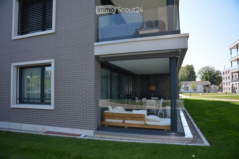 Balcony, wooden couch, dining table, green lawn, brick wall, glass windows