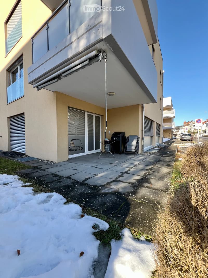 Front of the building with glass windows, balcony, storage boxes, small table, chair