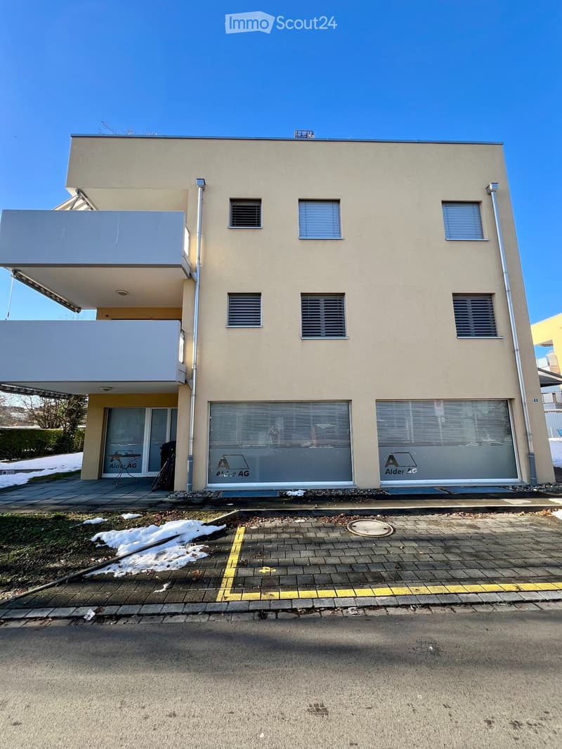 Modern residential building with three floors, large windows, terrace on the second floor, glass entrance doors, beige exterior walls