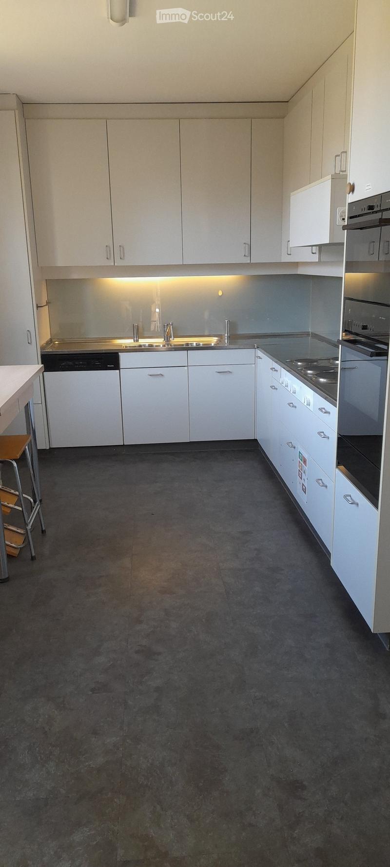 Modern kitchen with white cabinets, stainless steel appliances including a dishwasher, and a gray tile floor.