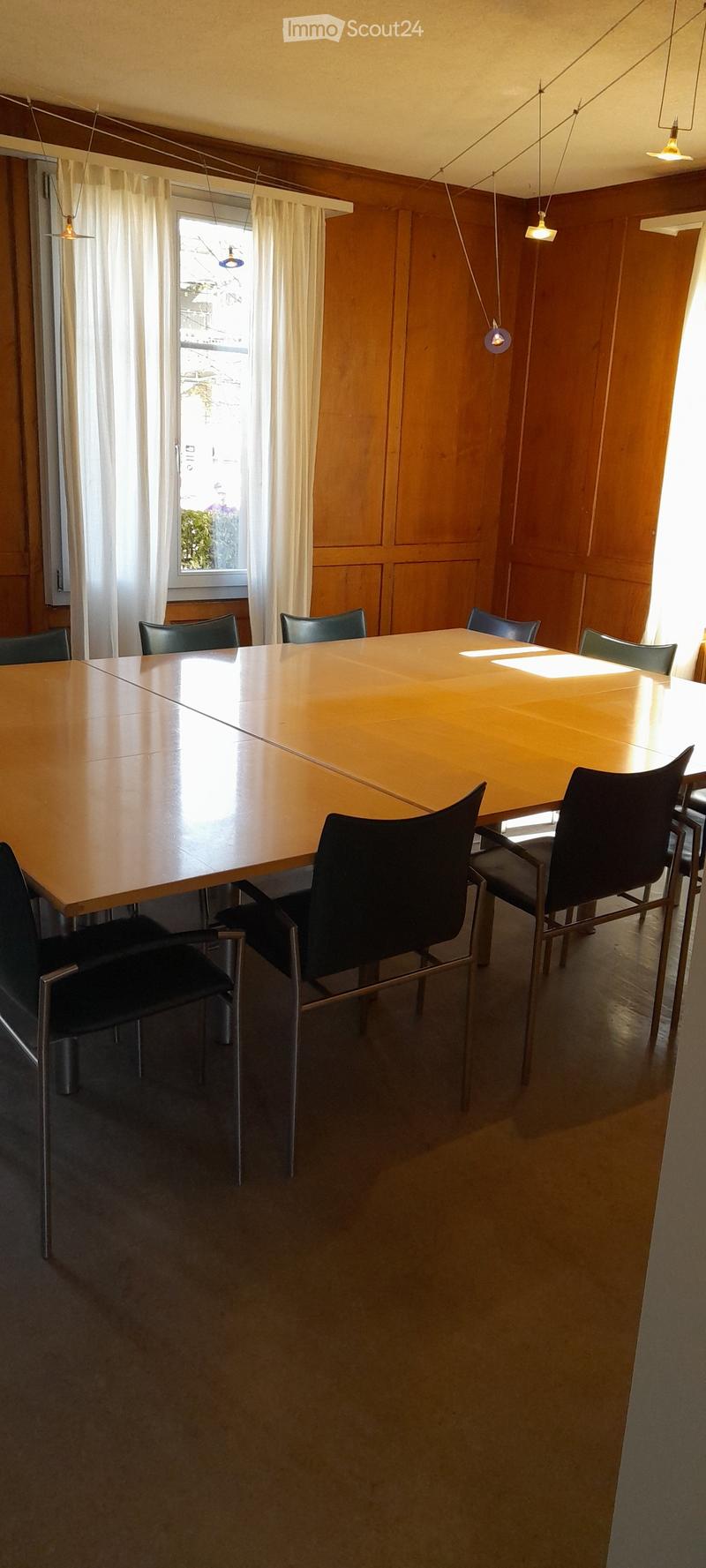 Large wooden dining table with black chairs, wooden paneled walls, large window, pendant lighting fixtures