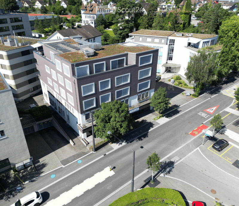 Aerial view of a multi-story building with several windows, a green roof, and an underground parking entrance.