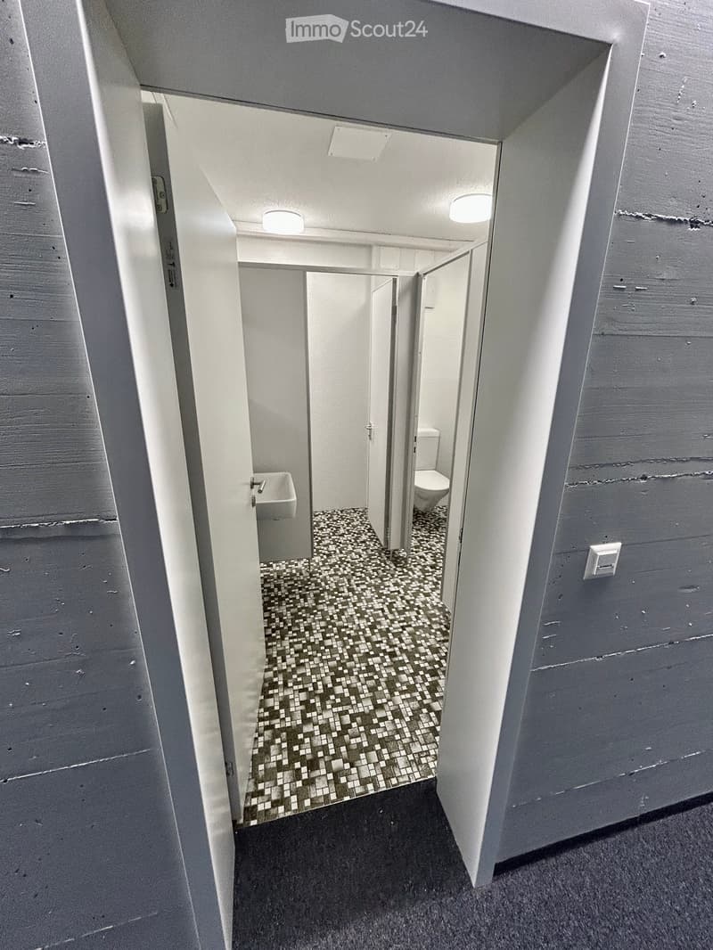 Small tiled bathroom with a sink and a toilet, open door, light on ceiling.