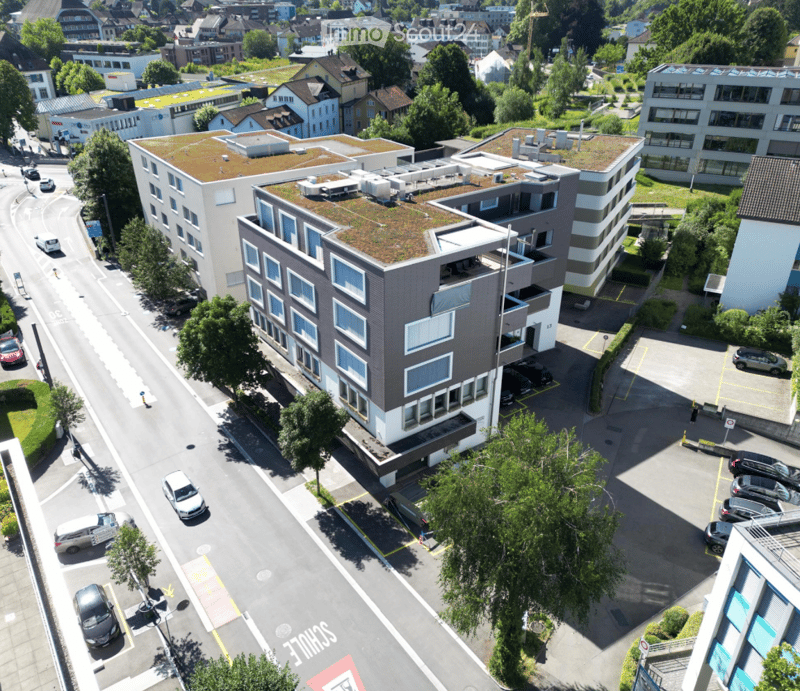 multi-storey building with green roof, several terraces, glass windows, and surrounded by cars and trees