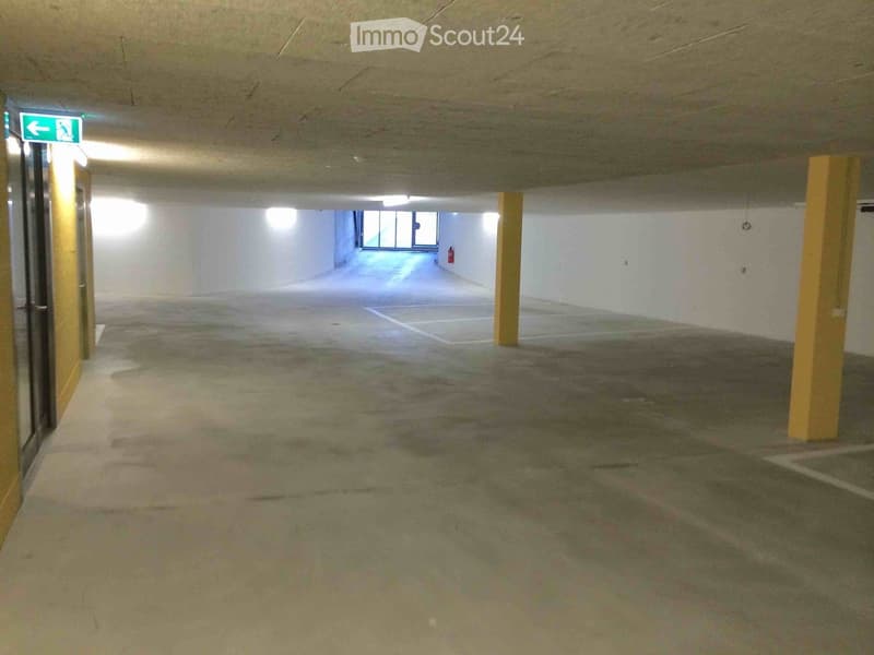 Empty basement parking lot with columns, entrance, and emergency exit sign