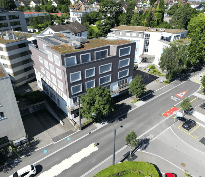 Aerial view of a multi-story building with several windows, a green roof, and an underground parking entrance.