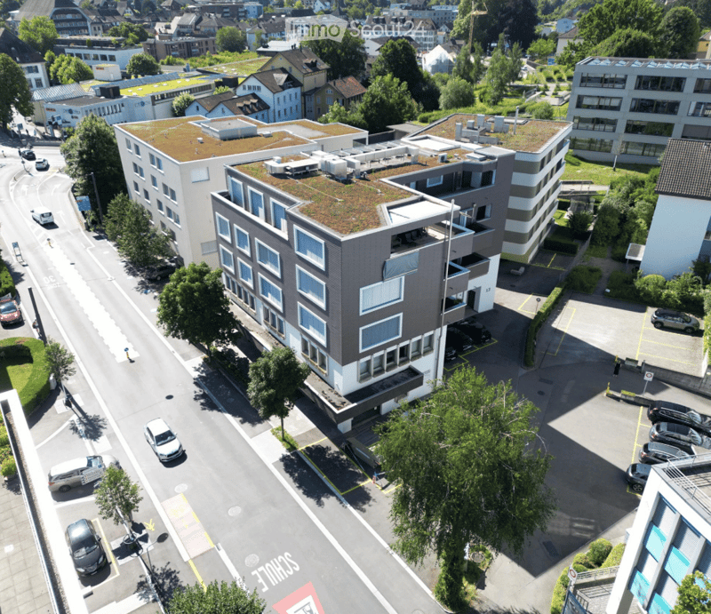 multi-storey building with green roof, several terraces, glass windows, and surrounded by cars and trees