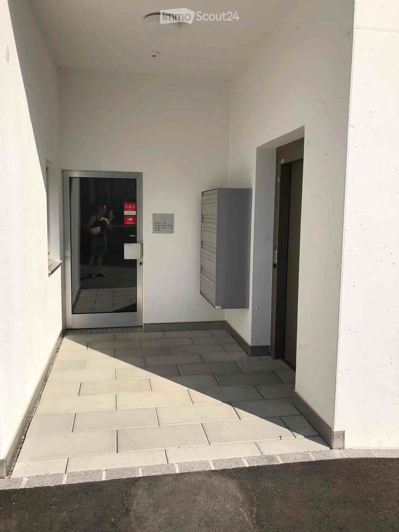 concrete walkway, mailboxes, elevator, glass door, white walls, red sign