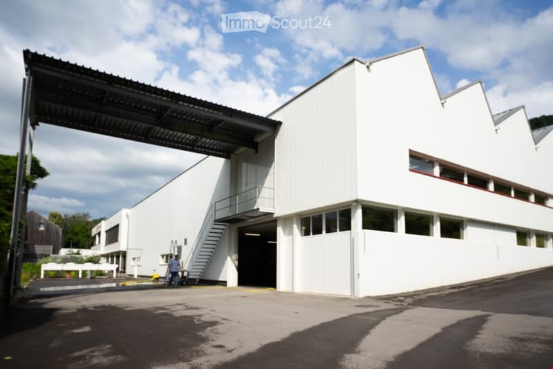 Modern white building, large entrance with staircase, a visible garage area, parking area in front