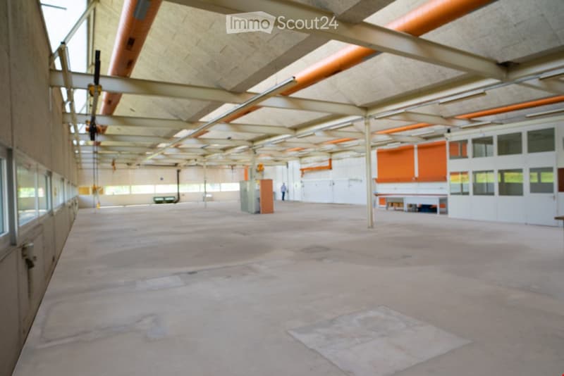 spacious, empty hall with high ceiling, metal beams, exposed pipes, concrete floor, large windows