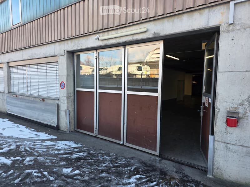 A concrete building with a glass entrance door, double garage doors, and snowy ground.