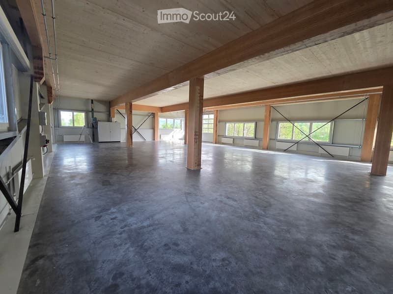Empty room with concrete floor, wooden beams, and large windows. No furniture or equipment.