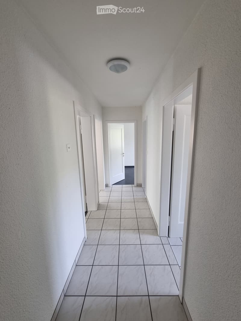 Corridor / Hallway. Empty hallway with white tiled floor and white walls. There are doors on both sides and a ceiling light.