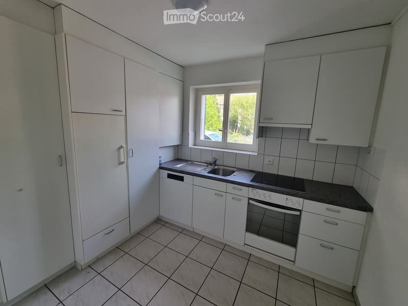 Kitchen. Modern kitchen with white cabinets, tiled floor, and a window with a view of trees outside.