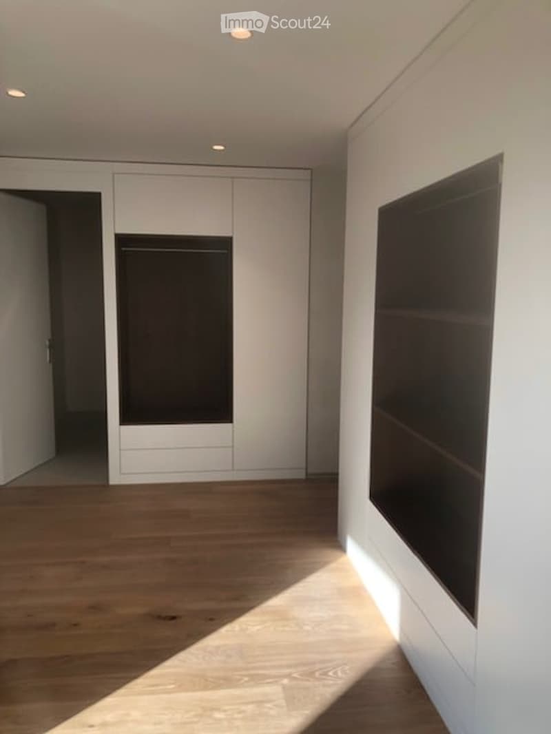 Empty room with hardwood floors, white built-in wardrobes, open closet, and a shelf with drawers