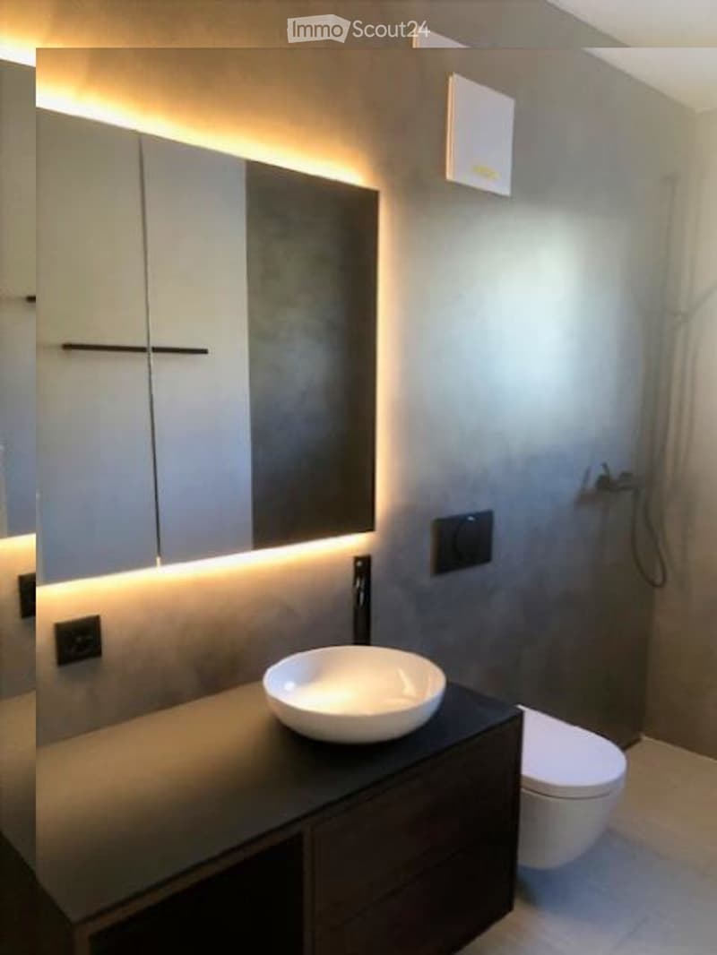 Modern bathroom with minimalist design, white fixtures, white ceramic sink, mirror above sink, light fixtures above mirror, white toilet