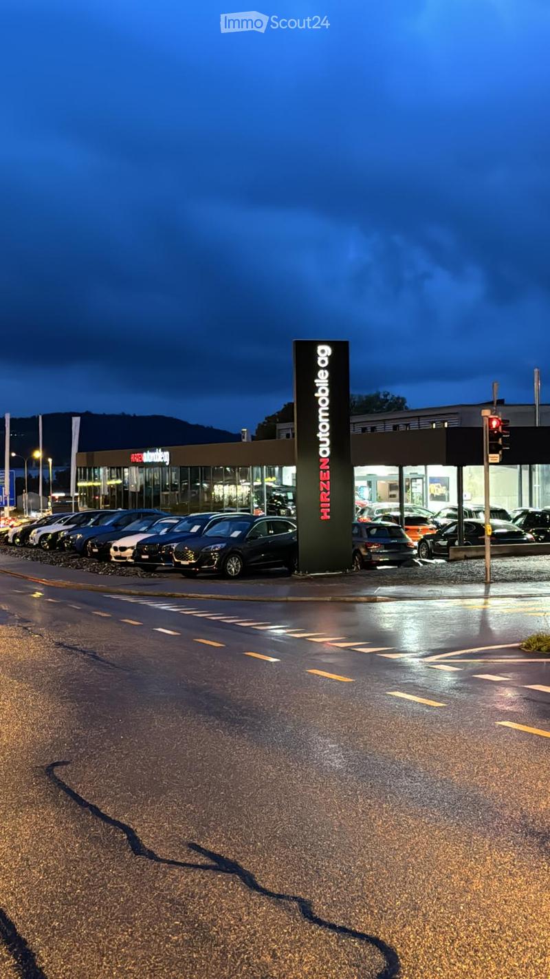 Commercial building, sign for a car dealership, multiple cars parked in front, dark blue night sky