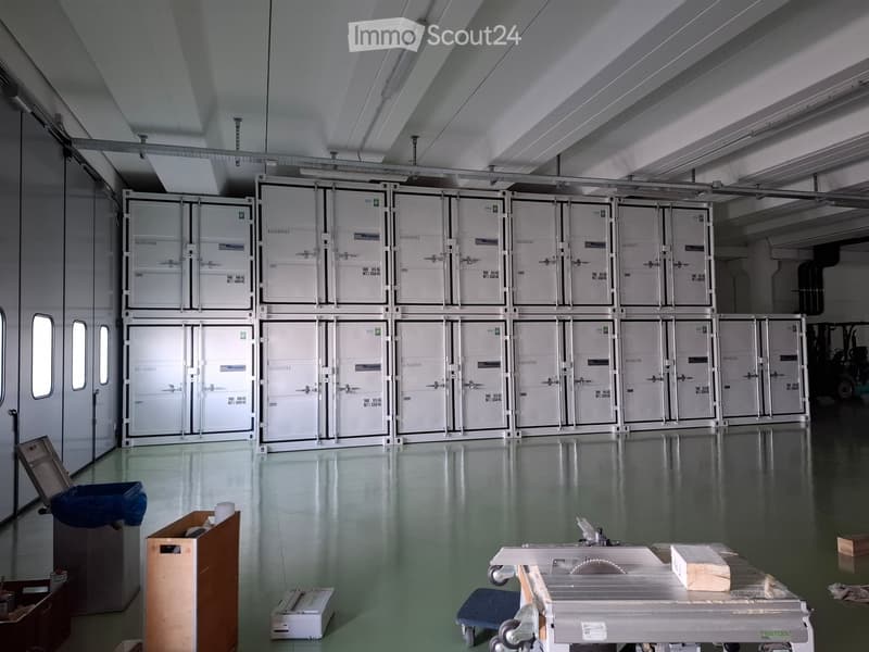 Warehouse with multiple storage containers, white walls, metal ceiling, green floor, and various equipment and boxes.