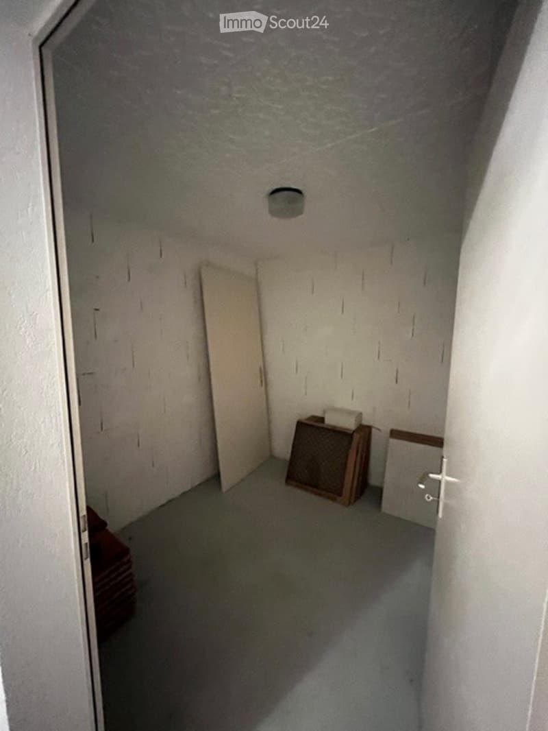 Empty room with gray floor, white walls, a ceiling light, two doors, and some wooden boxes