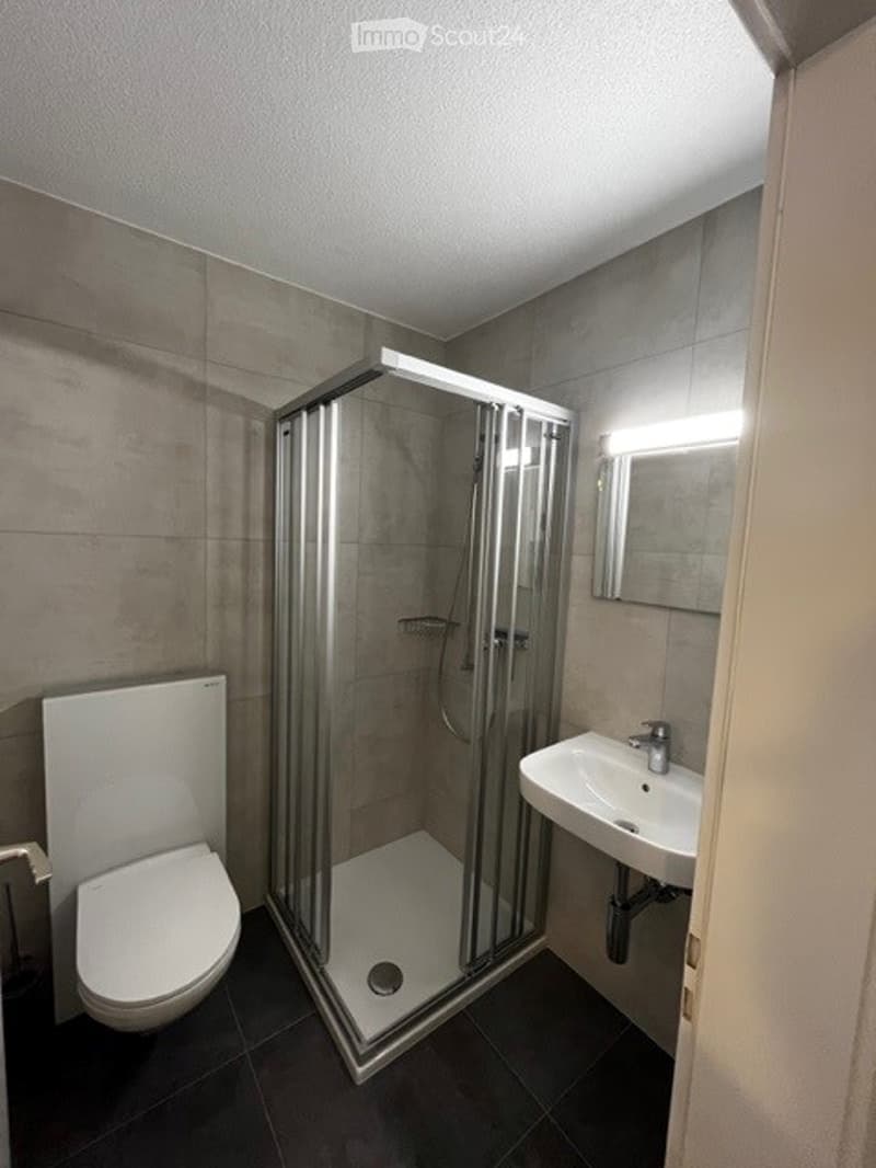 Modern bathroom with shower, sink, toilet, mirror, and tiled floor.