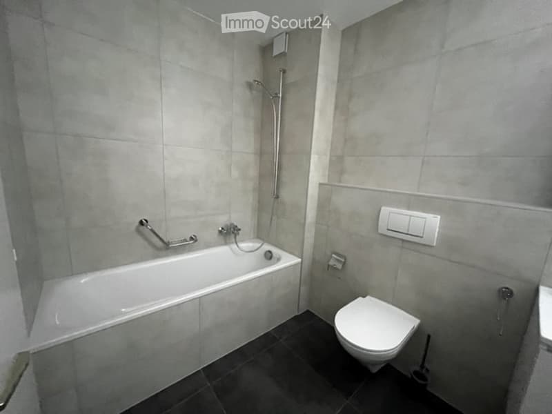 modern bathroom with white bathtub, toilet, shower, and gray tiled walls
