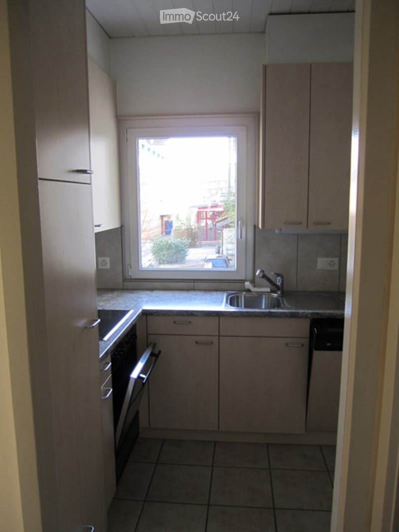 A small kitchen with a window, cabinets, and a countertop with a sink.