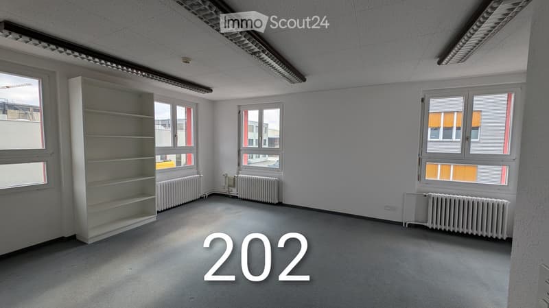 a vacant room with gray carpeted floor, three windows, and a shelf