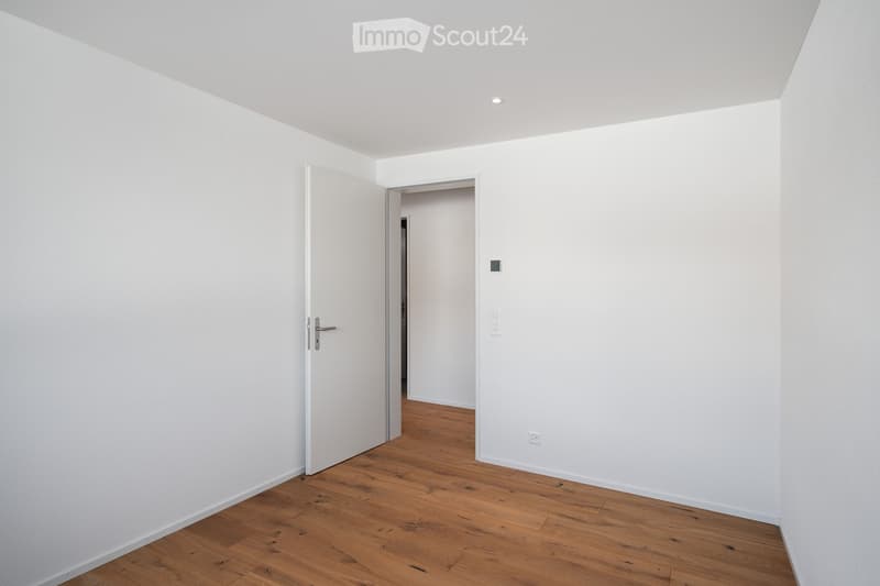Empty room with wooden floor, white walls, one door open