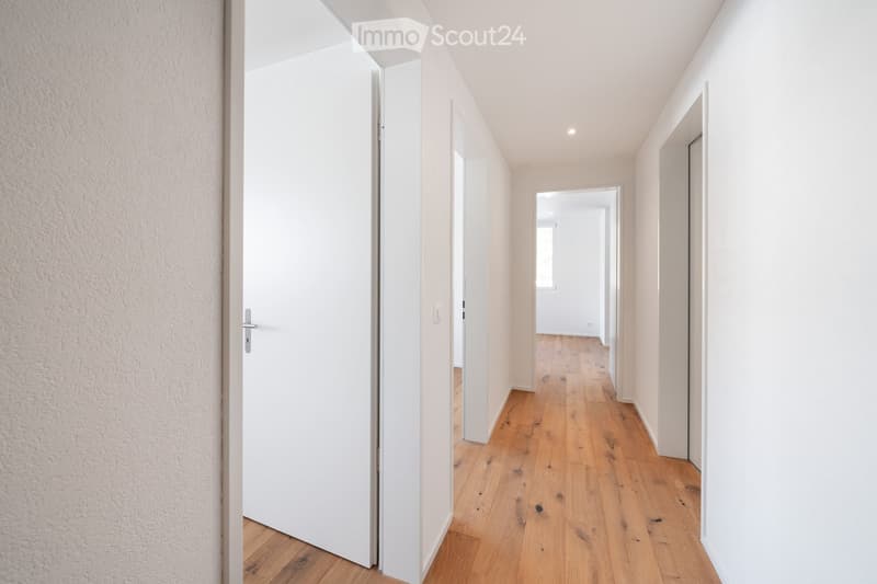 Empty corridor with white walls, wooden floor, and closed doors on both sides.