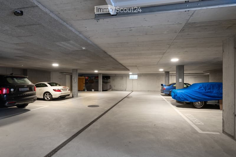 Underground parking with concrete walls, a white ceiling, and parked cars. The walls are covered with various storage boxes.