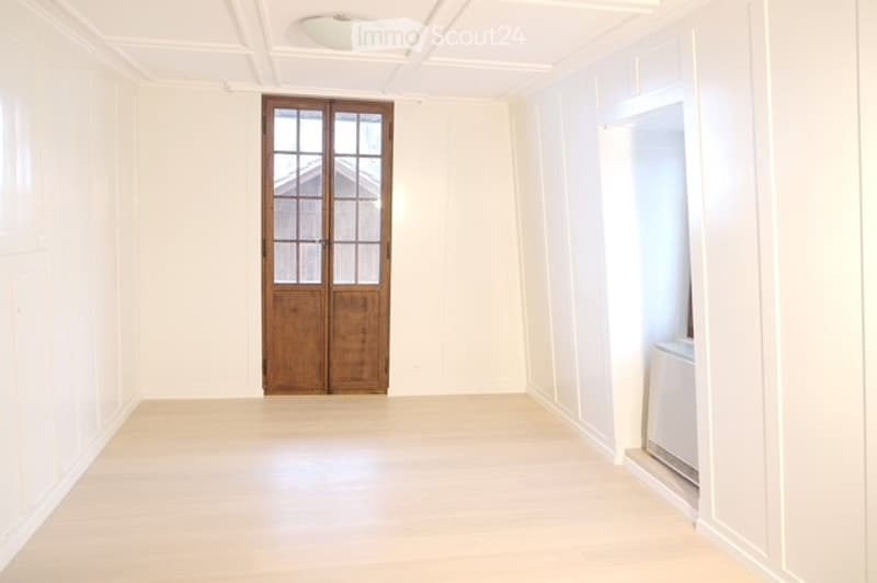Empty room, white walls, wooden door, wooden floors, white ceiling, washer in corner