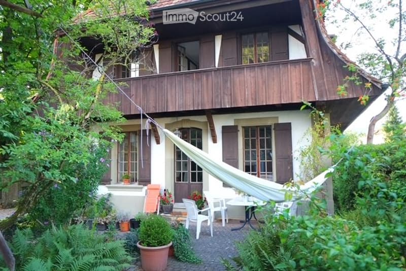 Half timbered house, white walls, brown wooden balcony, surrounded by plants and trees, garden