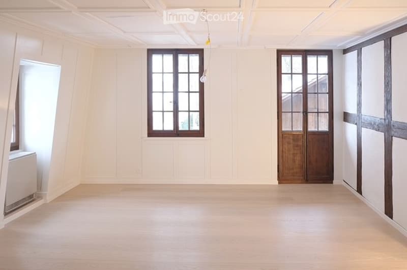 empty room, wooden door, two windows, wooden beams, white ceiling, light fixture