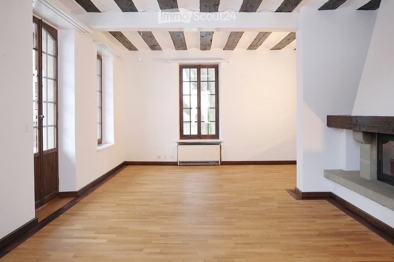 hardwood floors, fireplace, radiator, two windows, wooden beams on ceiling