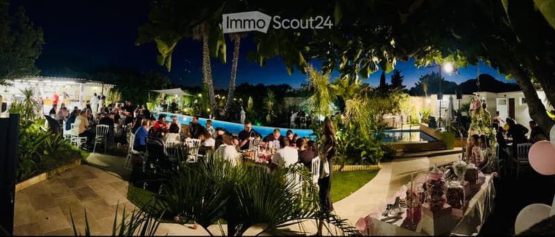 nighttime gathering, swimming pool, plants, people sitting around tables, balloons