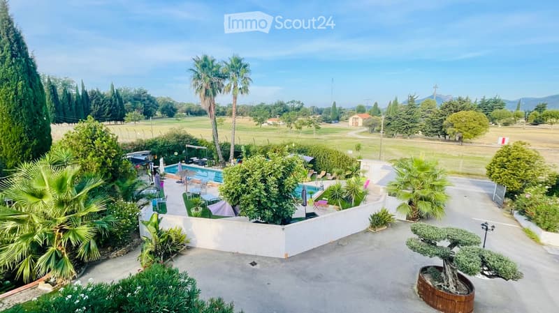 House with outdoor pool, wide garden with trees, road access with parking, golf course in the background.