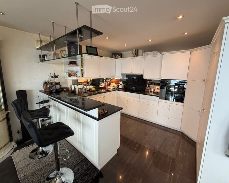 Modern white kitchen with black granite countertop, stainless steel appliances, bar stools, glass shelves, large room