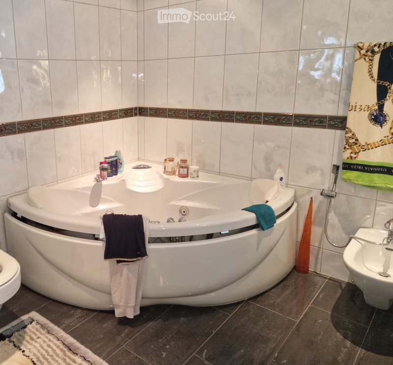 Large white bathtub, white tiled walls, sink, toilet, towel, white rug