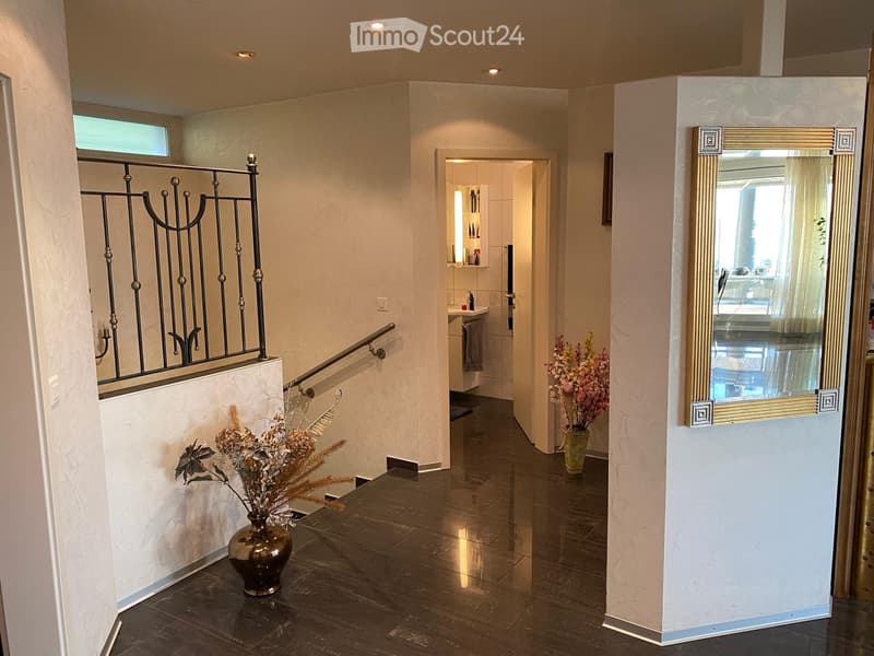 A hallway with a staircase, a mirror, and a vase with flowers