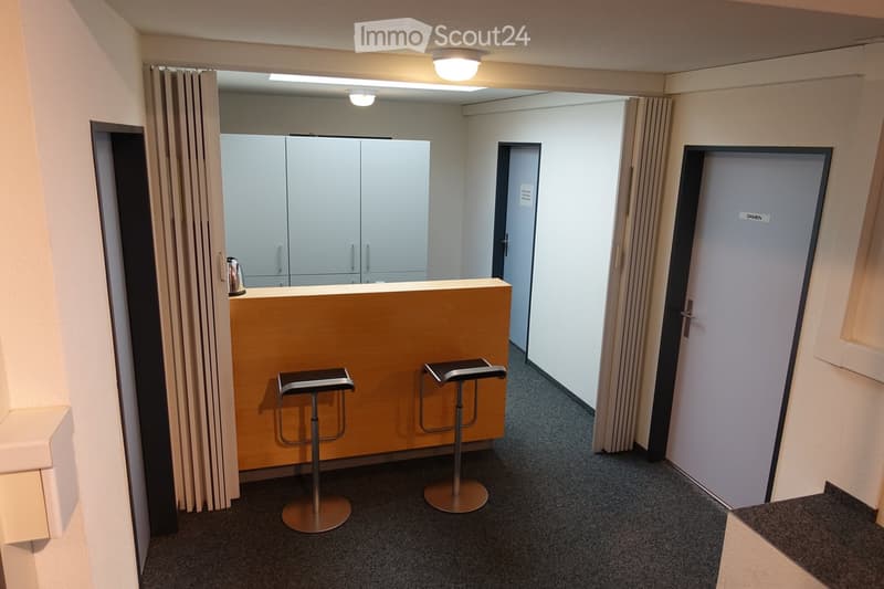 two stools, wooden counter, grey cabinets, ceiling lights, beige walls, dark grey carpet