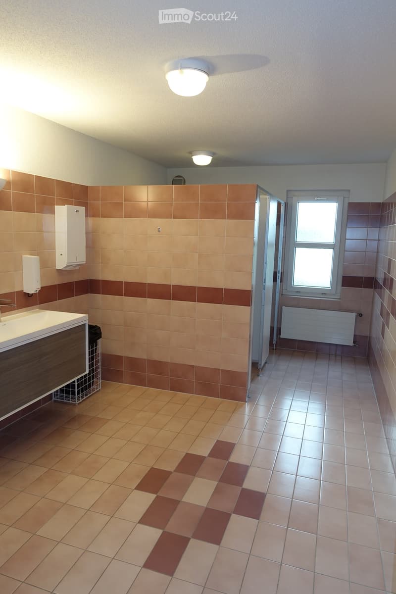 Clean tiled floors, sink with faucet, toilet stalls, wall mounted soap dispenser, ceiling lights