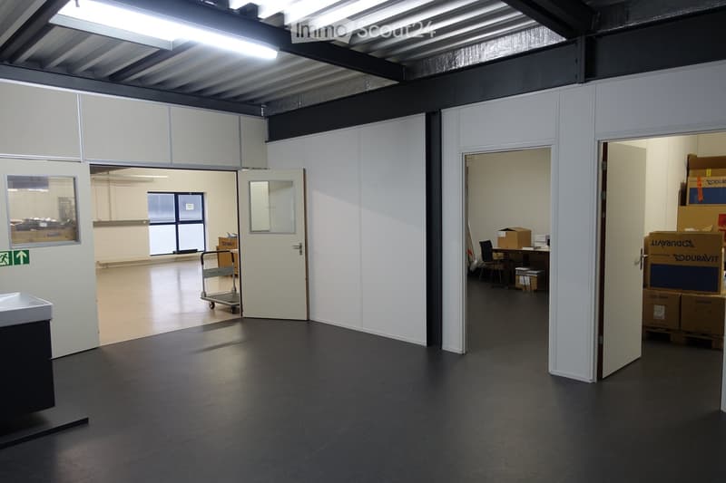 Large empty room with concrete floor, metal ceiling, and walls made of grey panels. Cart and several boxes.