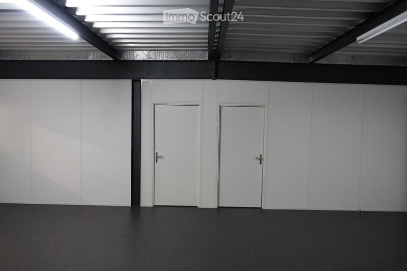 spacious, white walls, gray floor, two doors in the center, metal beams on the ceiling, two fluorescent lights