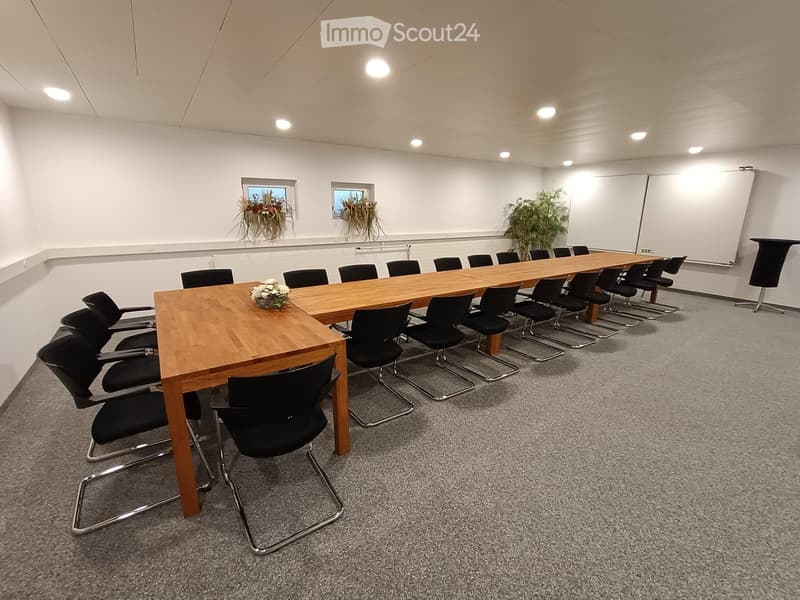 Long wooden table with black chairs on either side, two white boards on the wall, potted plants in the corner