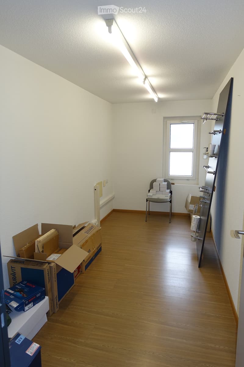 Empty room, wooden floor, fluorescent ceiling lights, chairs with boxes, open window, shelves with toilet paper and cups