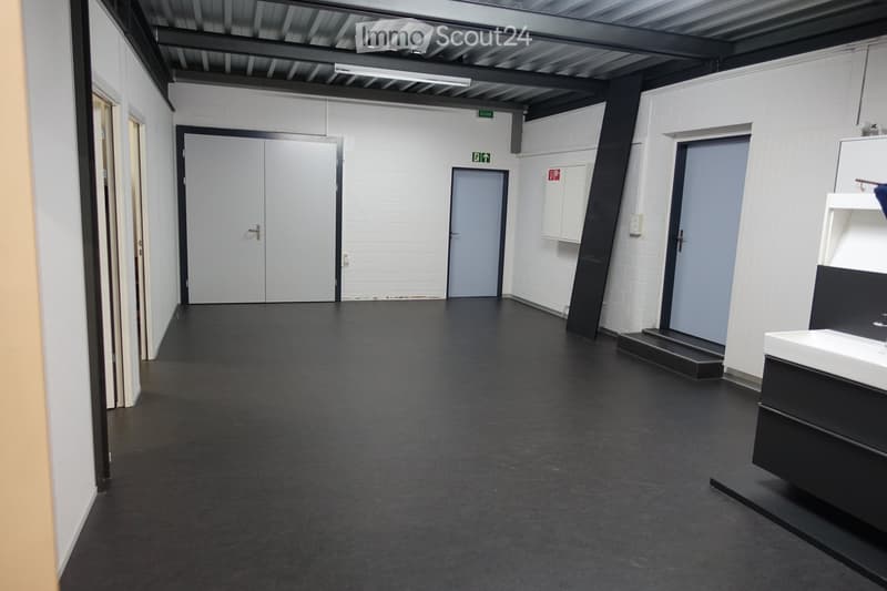 Large empty room, concrete floor, white walls, 2 doors, single fluorescent ceiling light