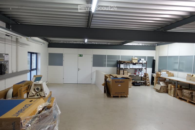 Wide warehouse space with white walls, gray dividers, large door, storage boxes, shelves, white flooring.