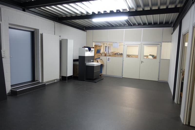 an empty room with white walls, black flooring, a gray door, white cabinet, metal ceiling with a lit up fluorescent light, and glass doors with windows.