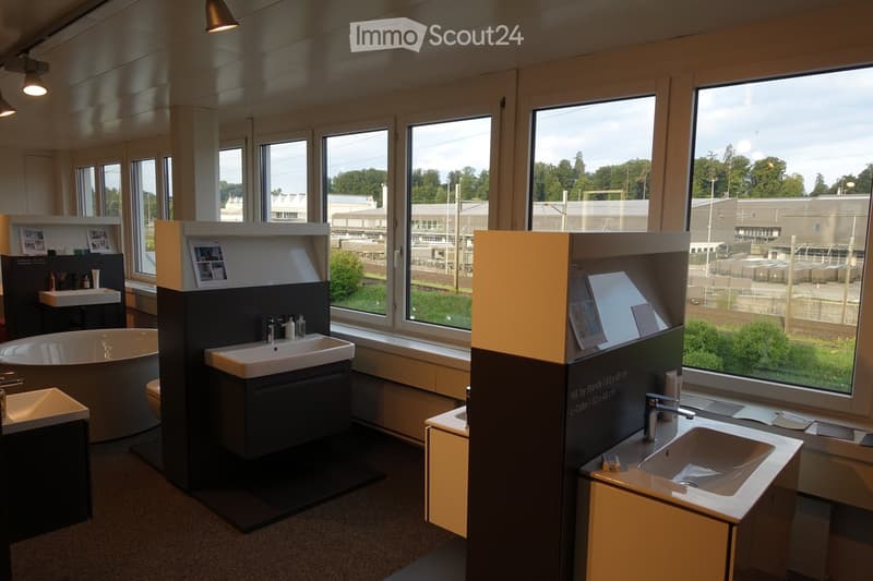 The image shows a bathroom showroom with various bathroom fixtures on display. The fixtures include bathtubs, sinks, toilets, and cabinets. There are three white bathtubs on display, with one in the center and two on the sides. There are also three sinks