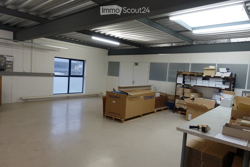 An empty warehouse space with white walls, metal ceiling, a door, a window, various storage boxes, and a shelf. The floor is polished and clean.
